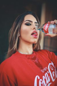 A estrat&eacute;gia amplia o conhecimento e percep&ccedil;&atilde;o da marca : influenciadora com camisa da coca-cola segurando uma garrafa da marca 