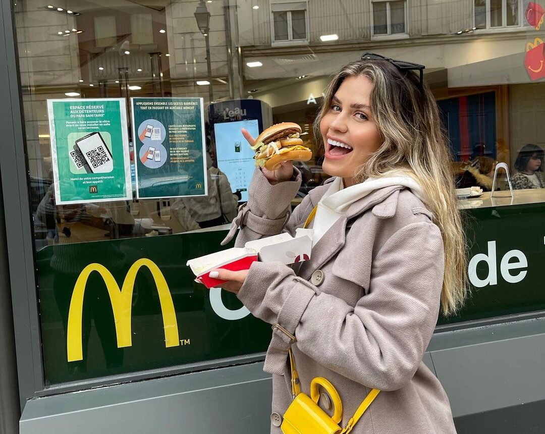 Influenciadora comendo Macdonald's em frente a uma loja