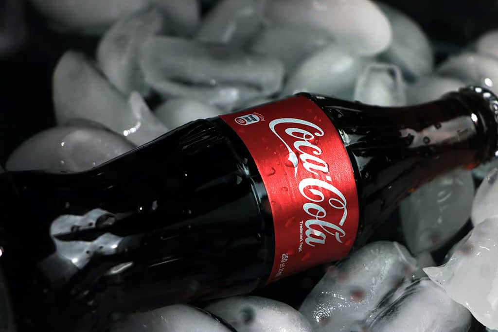 Exemplos de posicionamento de Branding : Garrafa de coca-cola de vidro deitada em torno v&aacute;rios cubos de gelo