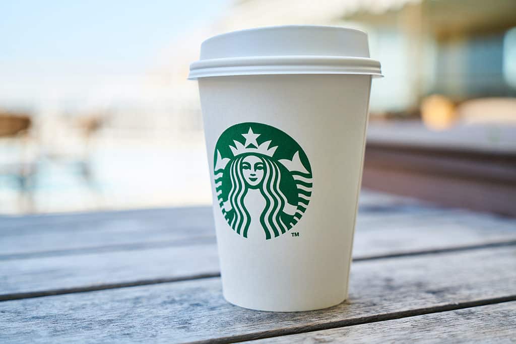 Exemplos de posicionamento de Branding : Um copo branco com a logo da Sturbucks em uma superficie de madeira