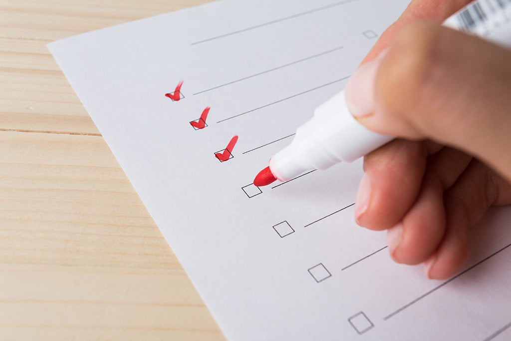 A import&acirc;ncia de um Instagrammer para o seu neg&oacute;cio : Uma m&atilde;o fazendo marca&ccedil;&otilde;es em uma lista com caneta vermelha