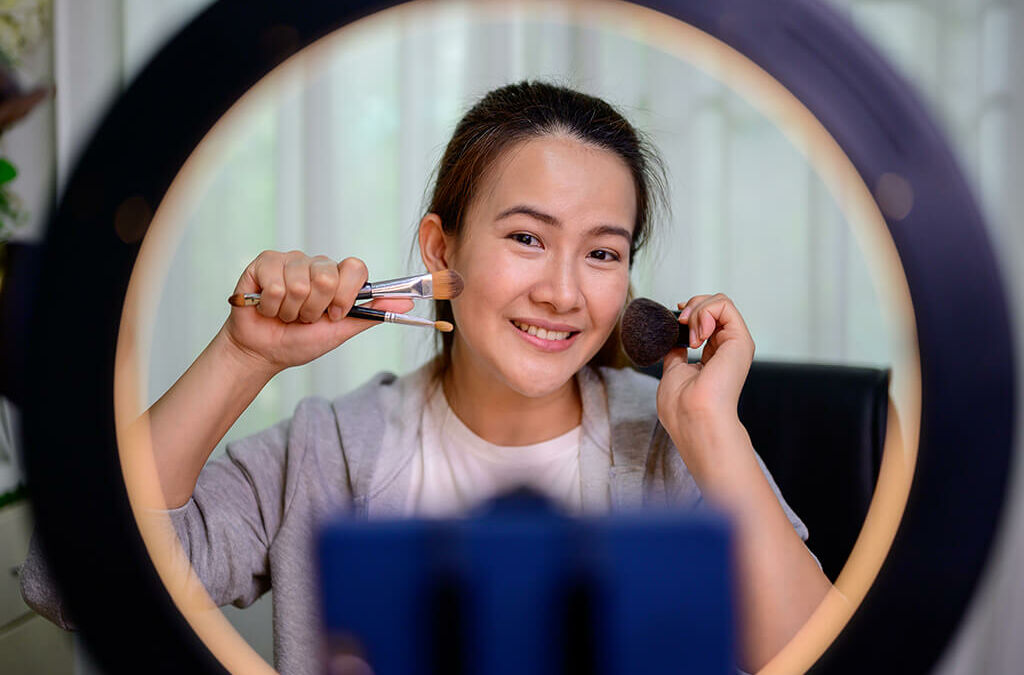 micro influencer asiatica femininacom pinceis encostando no rosto de frente uma luminária de maquiagem