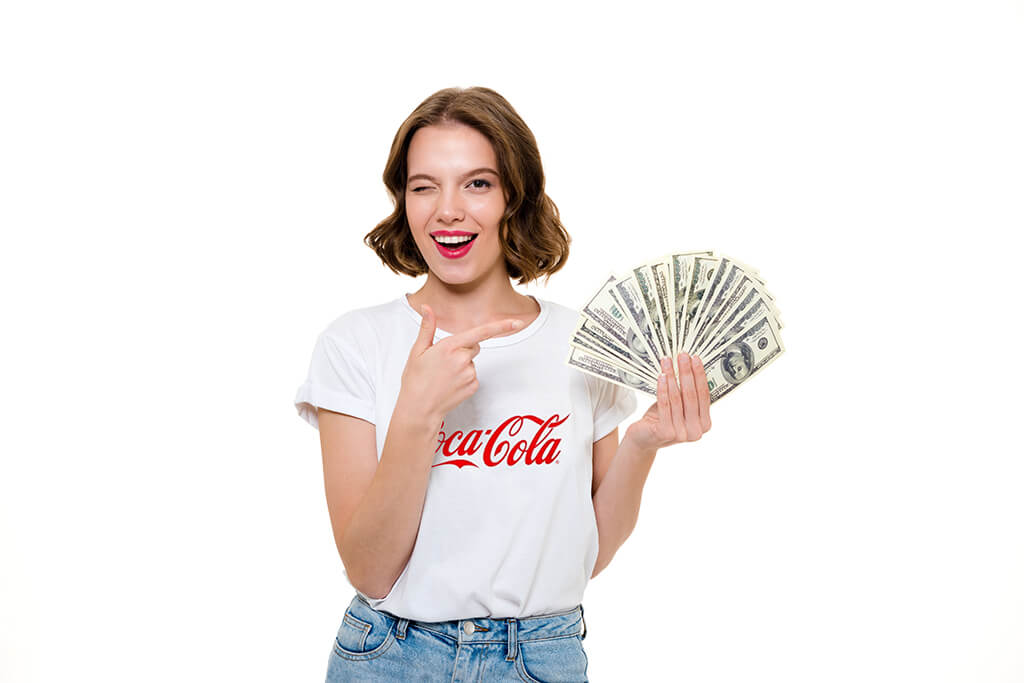 Por que muitas pessoas querem se tornar um influenciador digital? : Influenciadora digital com blusa branca da marca coca cola segurando um leque de dolares em uma das m&atilde;os