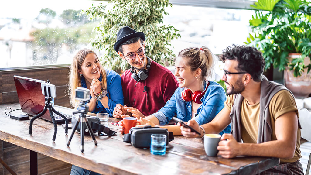 O que &eacute; preciso para ser um bom influenciador digital ? : Influenciadores esntados juntos em uma mesa com celular e notebook pra grava&ccedil;&otilde;es