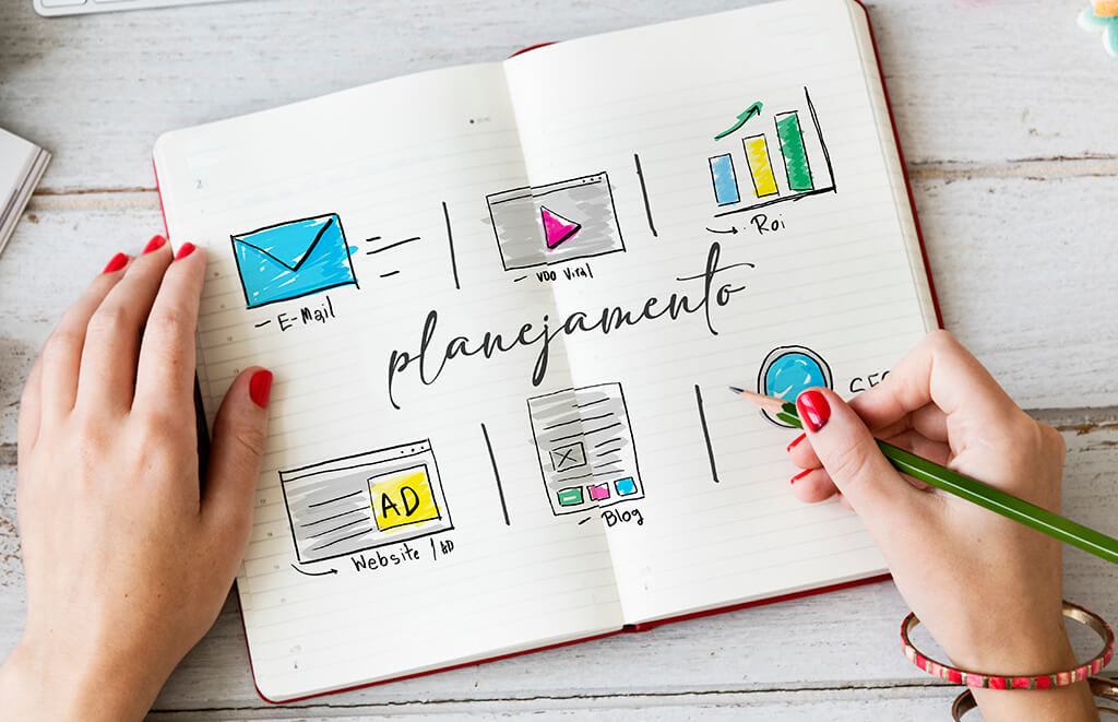 Como criar conte&uacute;do digital? : M&atilde;os femininas sob um caderno com escritos e desenhos de planejamento