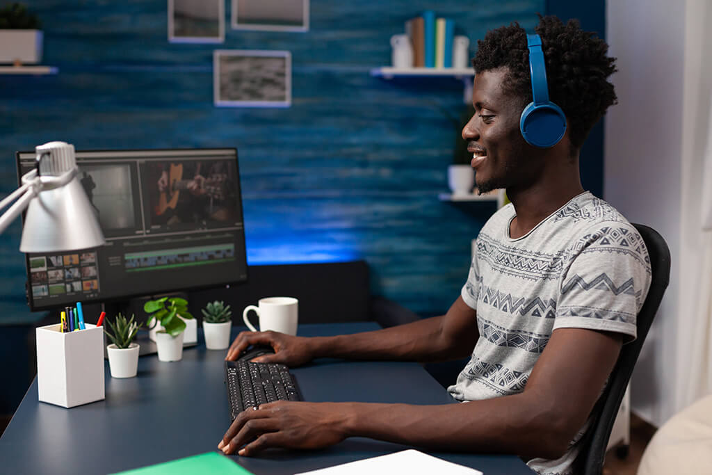 Tipos de conte&uacute;do digital : v&iacute;deo : Rapaz sentado em uma cadeira de frrente uma mesa com um computador com atela aberta num software de edi&ccedil;&atilde;o de v&iacute;deos